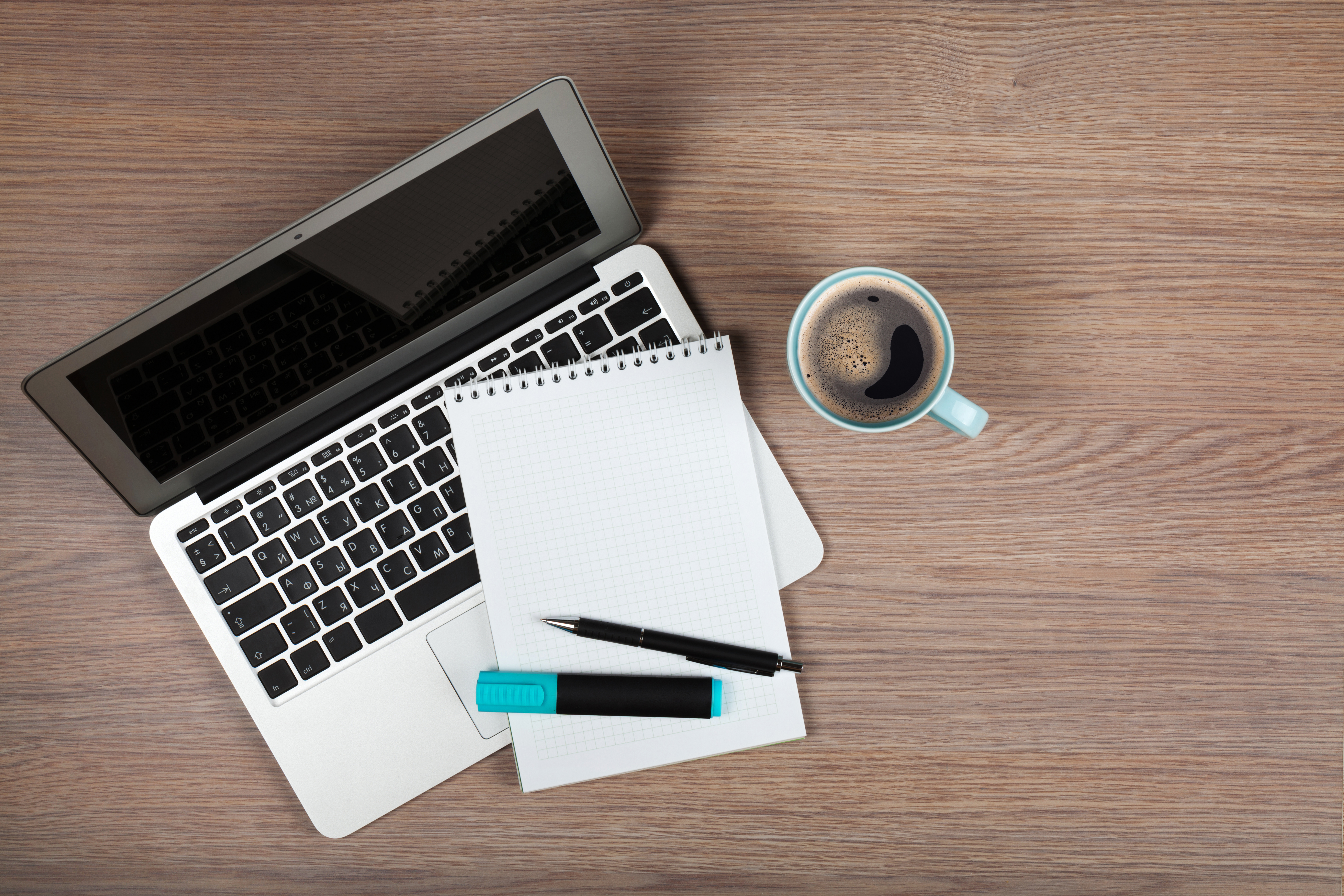 Blank notepad over laptop and coffee cup on office wooden table